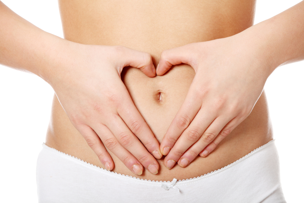 Person mit auf Bauch gelegten Händen, die Finger formen ein Herz