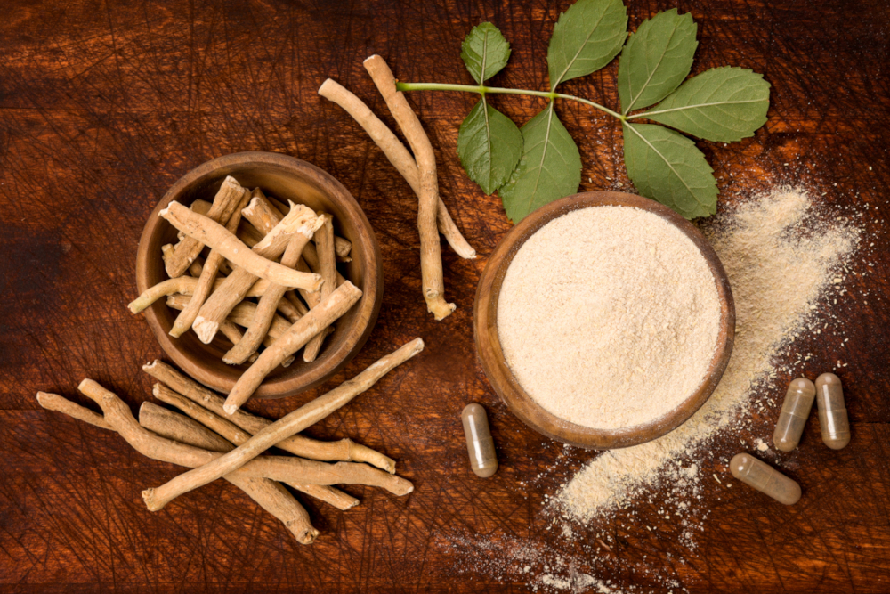 Roots, powder and leaves of ashwagandha as well as dietary supplement capsules on a dark wooden surface