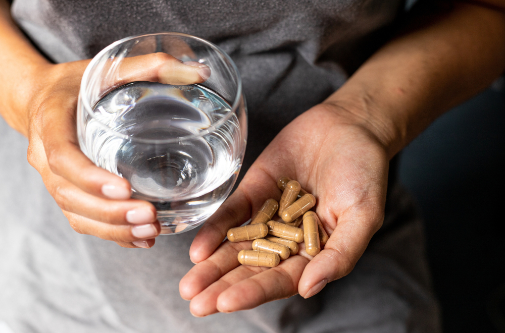 One hand holding several capsules, another holding a glass of water to take them