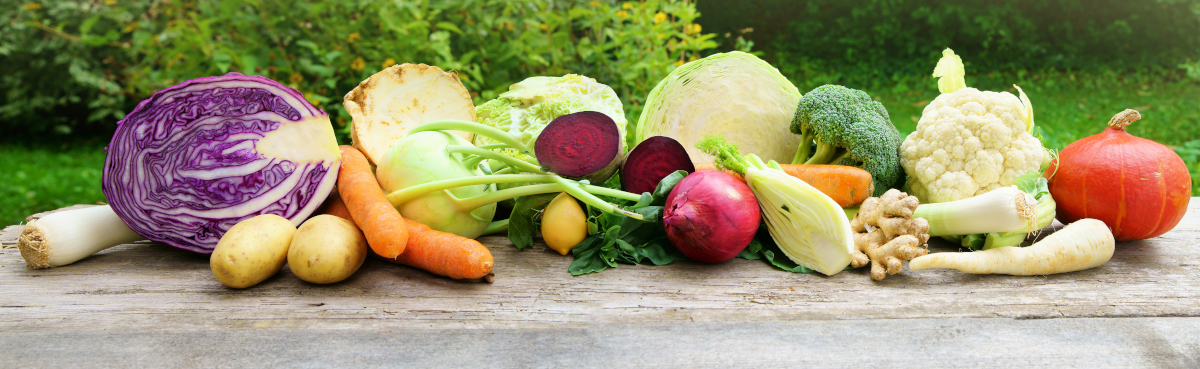 Verschiedene Gemüsesorten, darunter Kohl, Kürbis und Kartoffeln, auf einem Holzbrett in der Natur