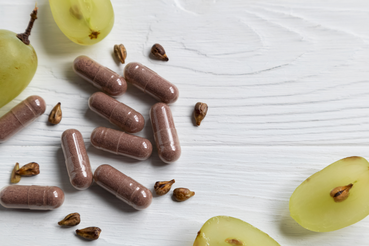Dietary supplement capsules, grape seeds and halved grapes on light wood
