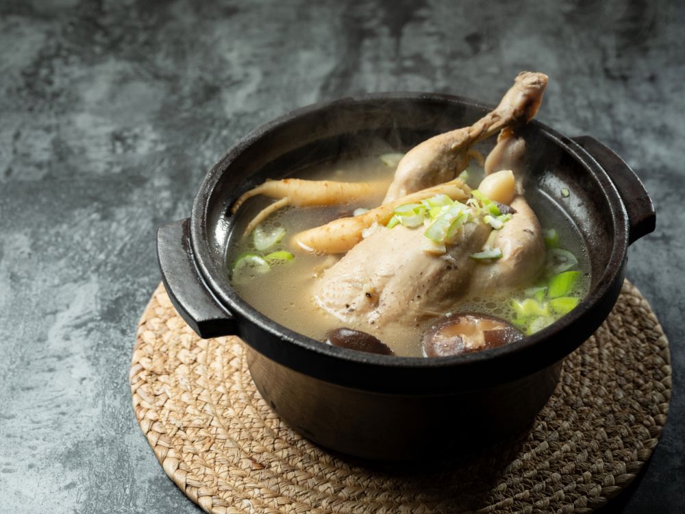 Asian clear soup with poultry, mushrooms, herbs and ginseng root on round cork mat