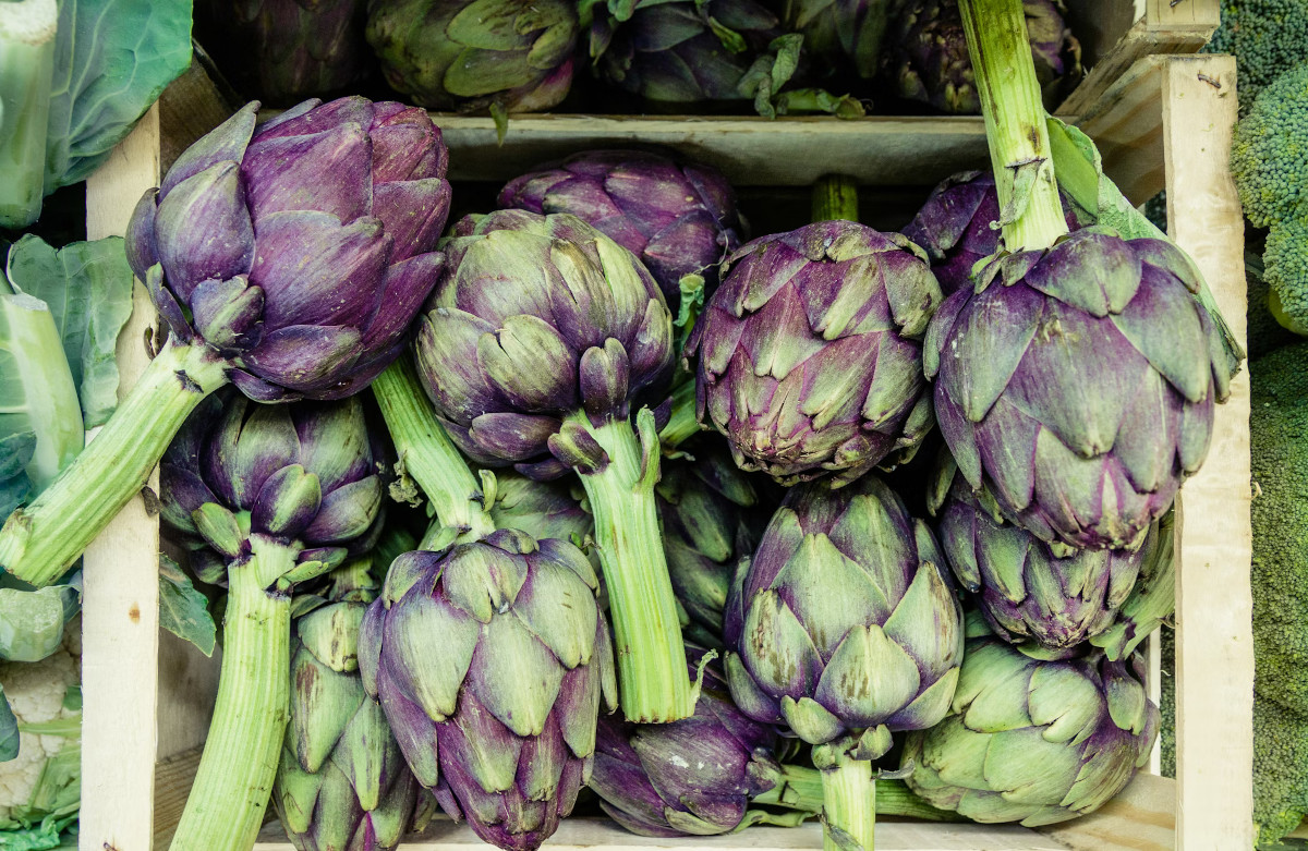 Artichokes in a wooden crate next to other vegetables