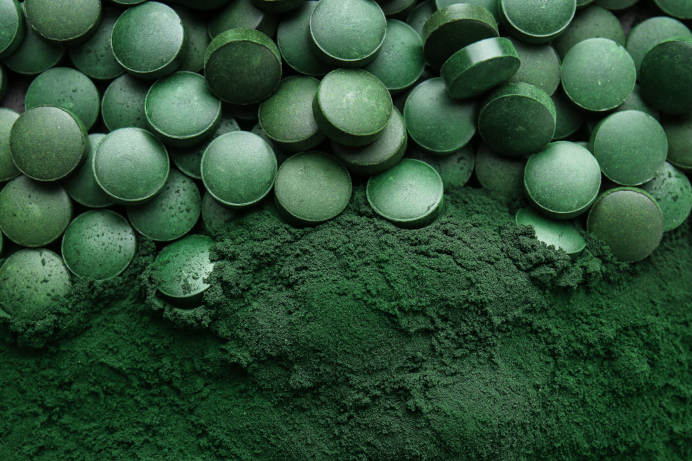 Spirulina tablets in the upper half of the image lie on Spirulina powder