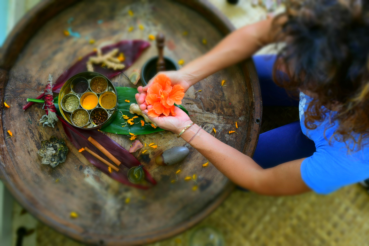 Person at a round wooden table with spices and utensils used in Ayurveda