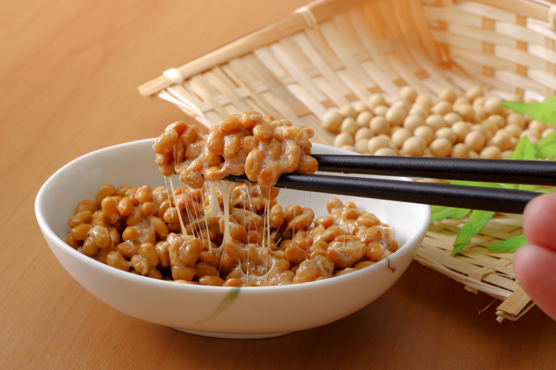 White bowl of Natto, with strings stretching between the portion on the chopsticks and the portion in the bowl.