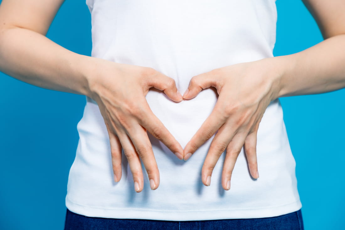 Person holding hands in a heart shape over the stomach