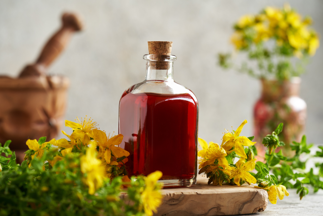 Red oil in a bottle on a wooden board, surrounded by St John's wort flowers.