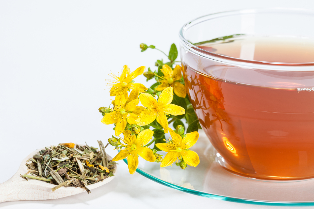A cup of orange-yellow St John's wort tea, with dried St John's wort and a flower as decoration.