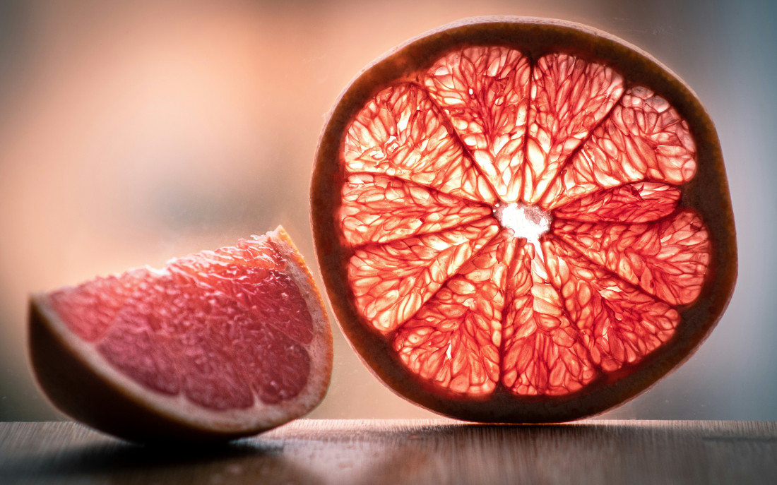 Photo of a standing grapefruit slice backlit, next to a grapefruit segment