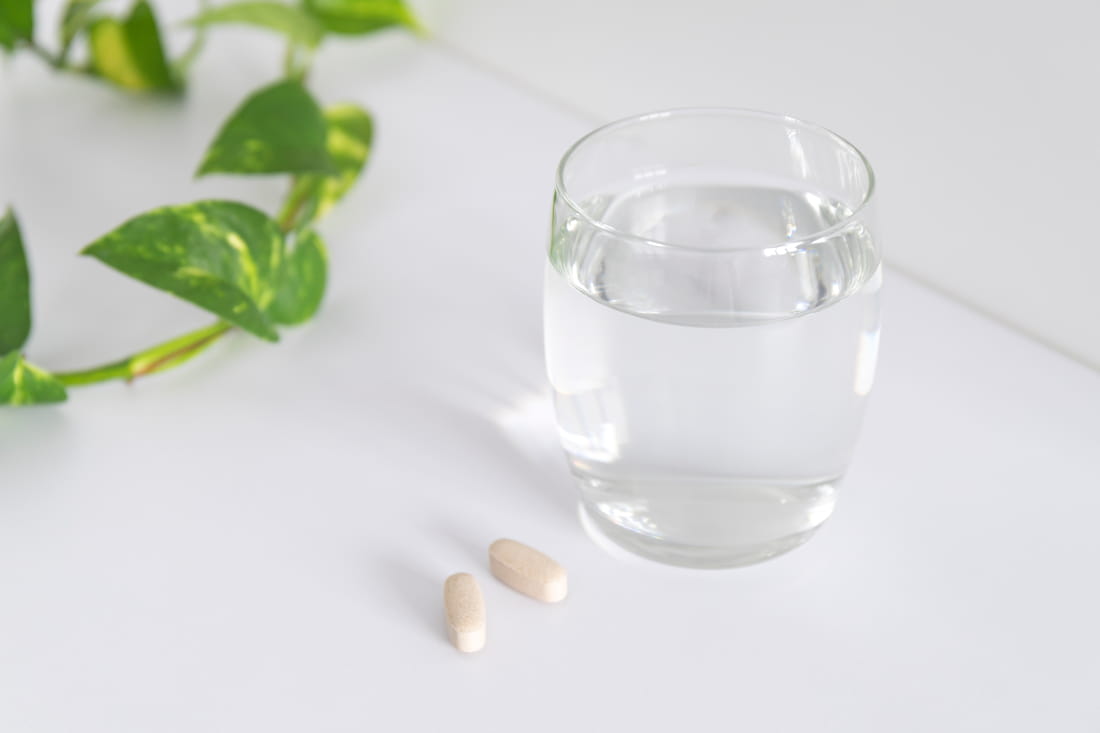 A glass of water, beside it two tablets and a green sprig with two leaves as decoration
