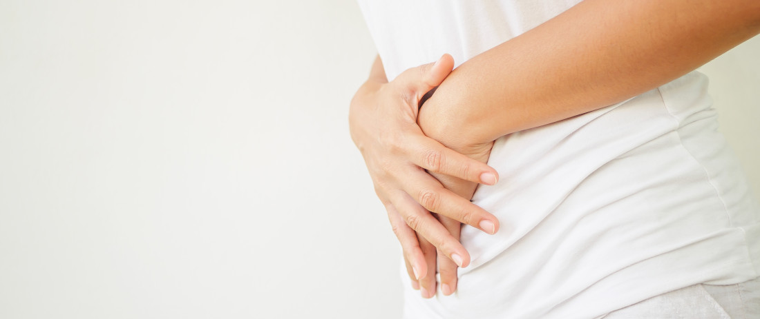 Person holding her hands over her abdomen. Close-up side view of the hands.