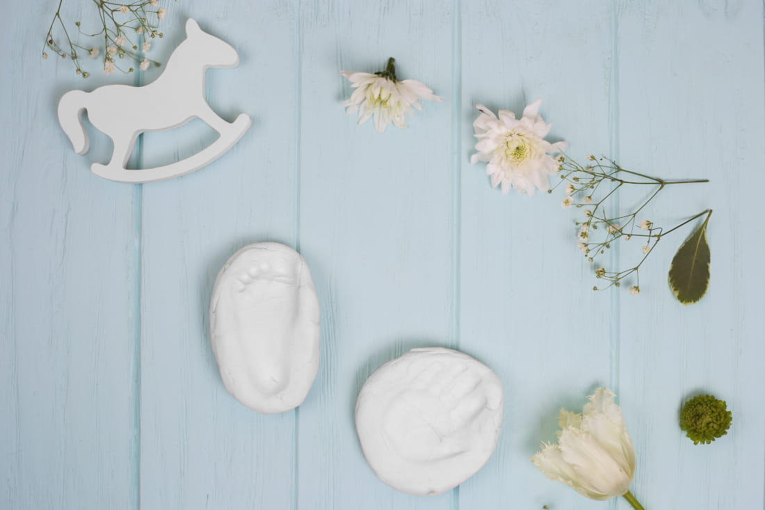 Plaster cast of hand and foot on white wood, wooden rocking horse and white tulip as decoration.