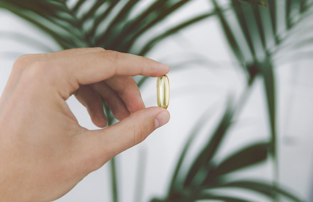 Hand hält eine gelbe Kapsel zwischen Daumen und Zeigefinger