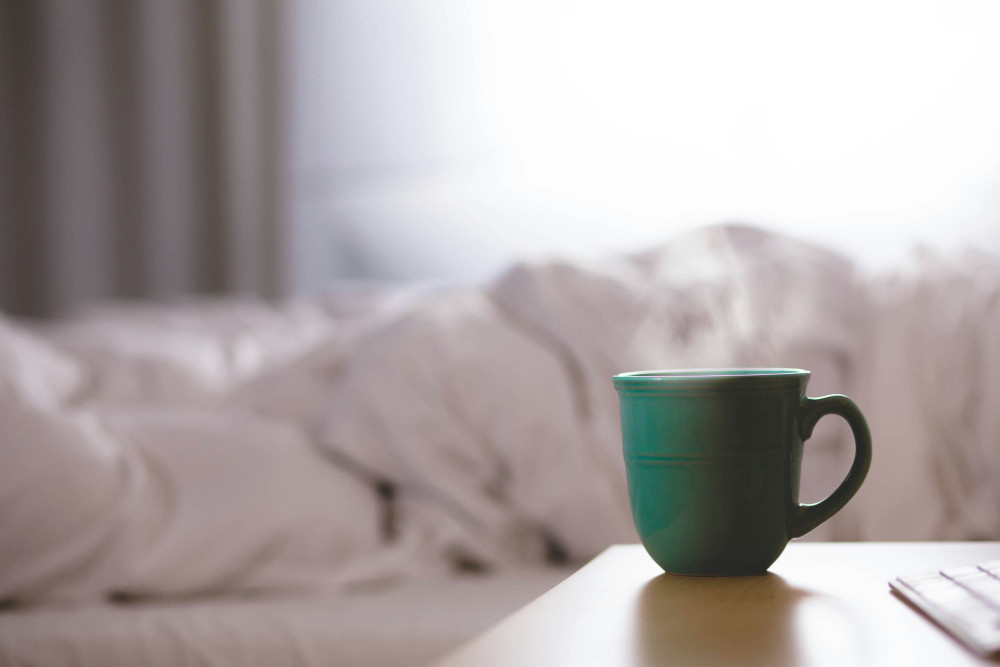 Tasse verte sur une table, en arrière-plan du linge de lit flou.