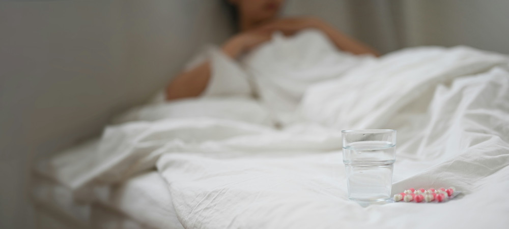 Personne au lit, verre d'eau avec gélules à côté
